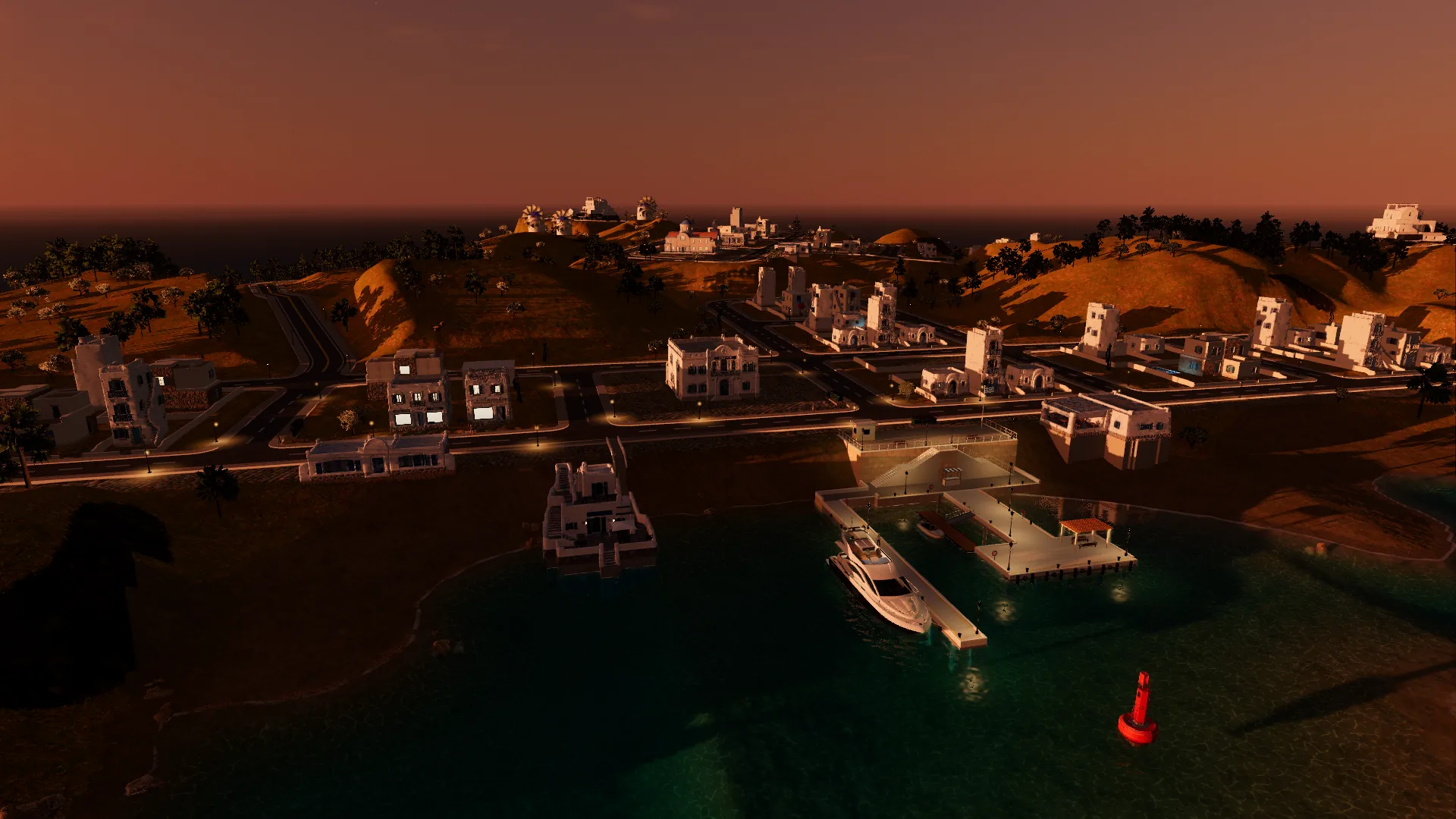 The same harbour at dusk with street lamps and lit windows, the yacht at the pier and the church and windmills on the skyline